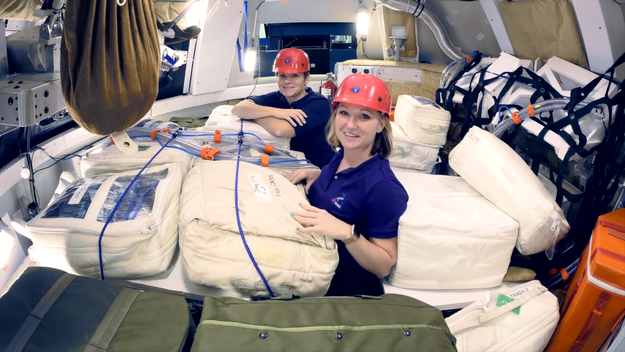 Jessica Vos e a astronauta Anne McClain dentro de uma cabine Orion representativa, cercadas por bolsas de estiva posicionadas para formar um abrigo contra radiação durante um evento de partículas solares.