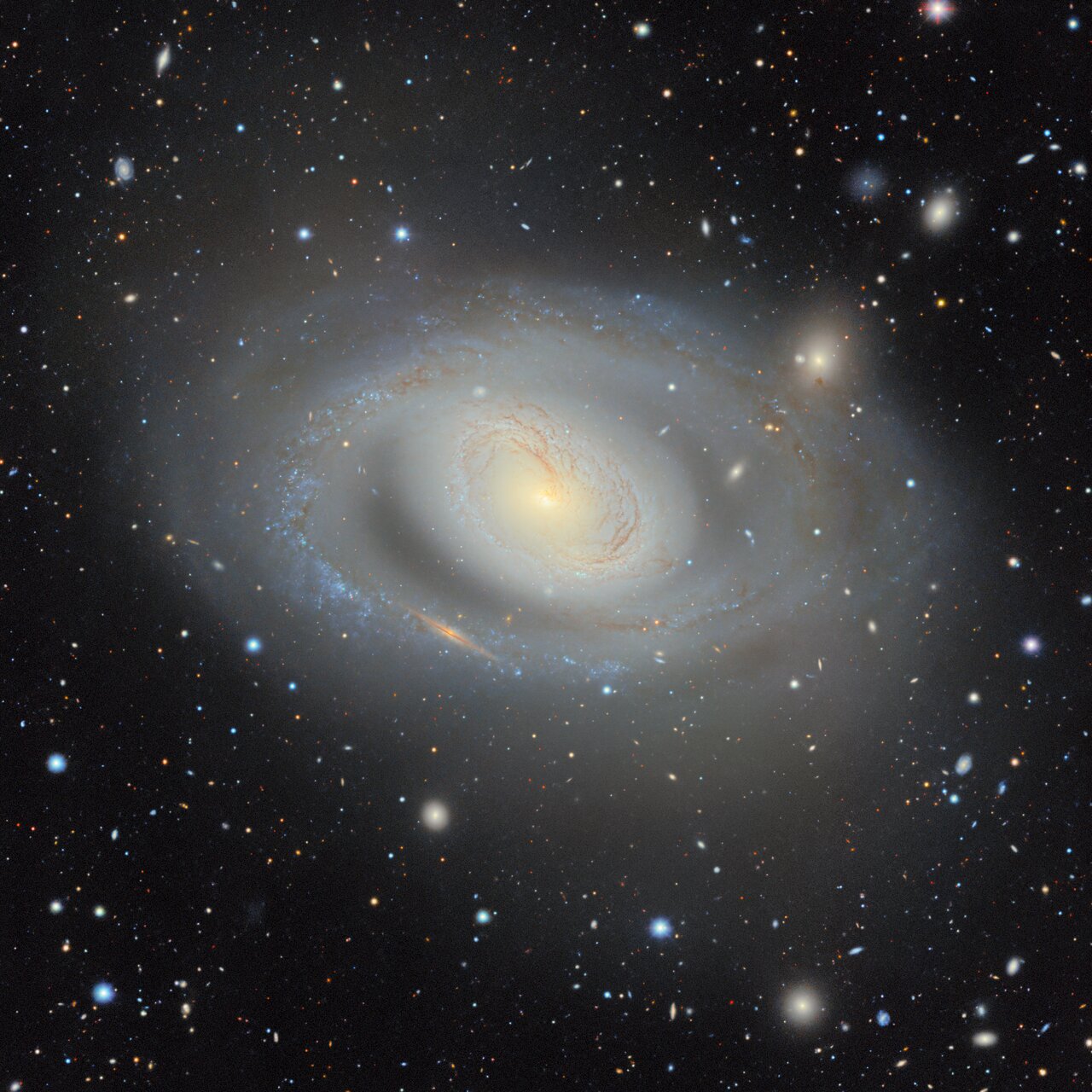 A galáxia espiral Messier 96 aparece em um campo escuro, cercada por estrelas e galáxias distantes.