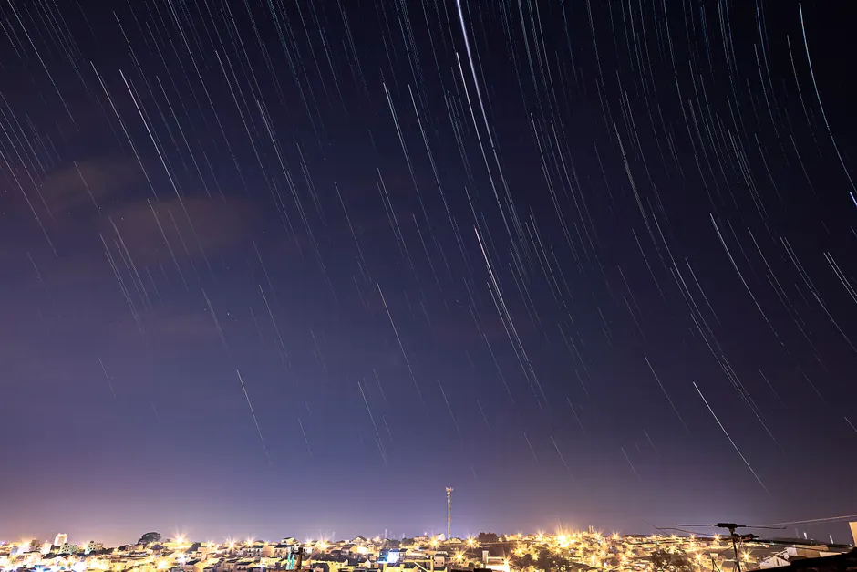 Foto de longa exposição de trilhas estelares sobre a paisagem iluminada da cidade de São Paulo à noite.