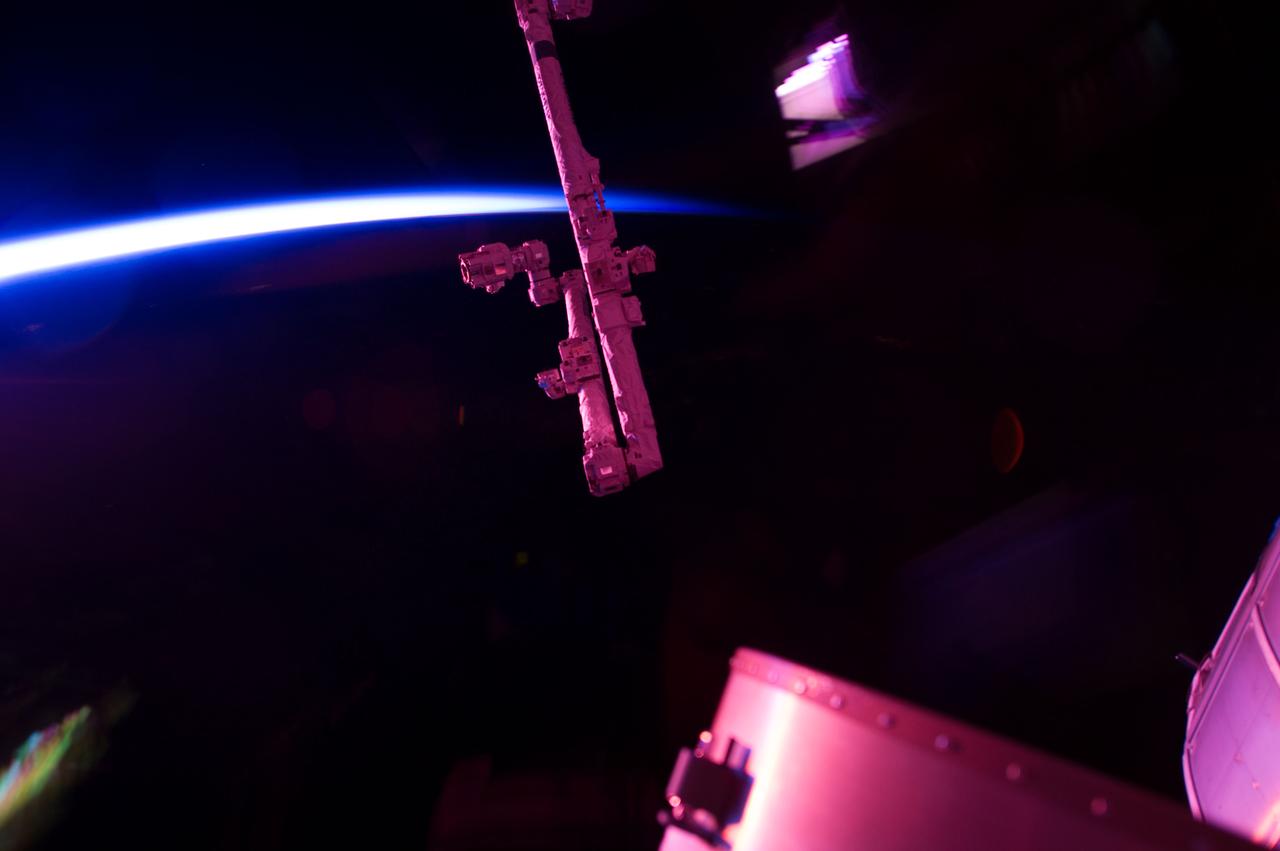 Borda noturna da Terra vista da Estação Espacial, cercada por finas faixas vermelhas e verdes do brilho natural da atmosfera.