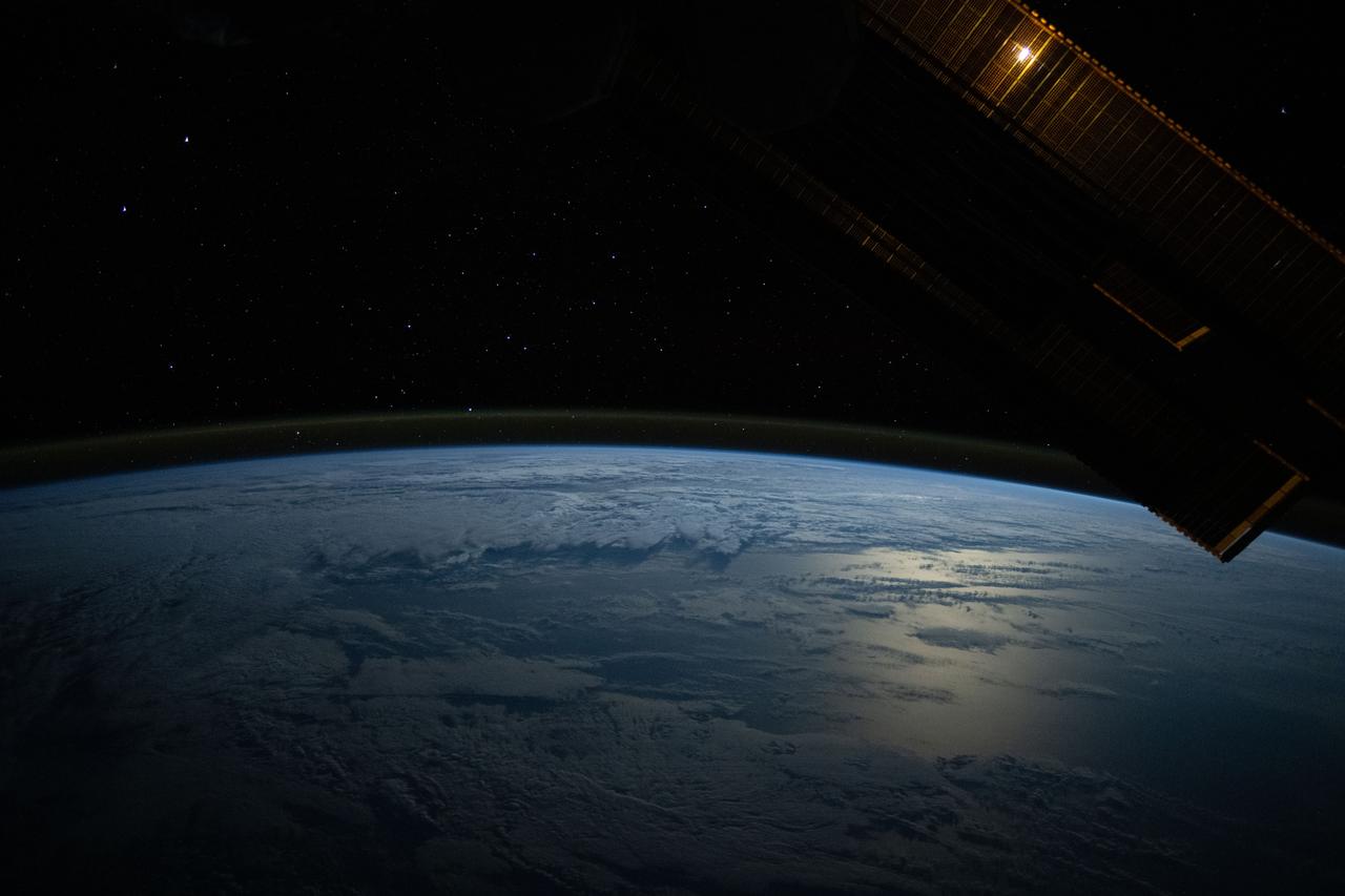 The Moon's glint beams off the Pacific Ocean as stars glitter in the background above the Earth's airglow. The Moon is obscured behind a solar array in this photograph from the International Space Station as it orbited 264 miles above.