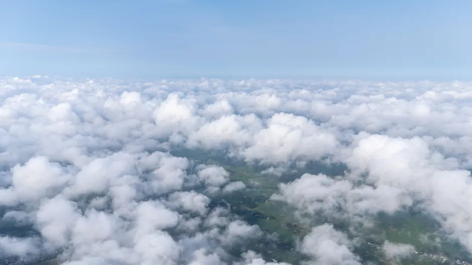 Uma serena foto aérea de nuvens fofas flutuando sobre paisagens verdes sob um céu azul claro.