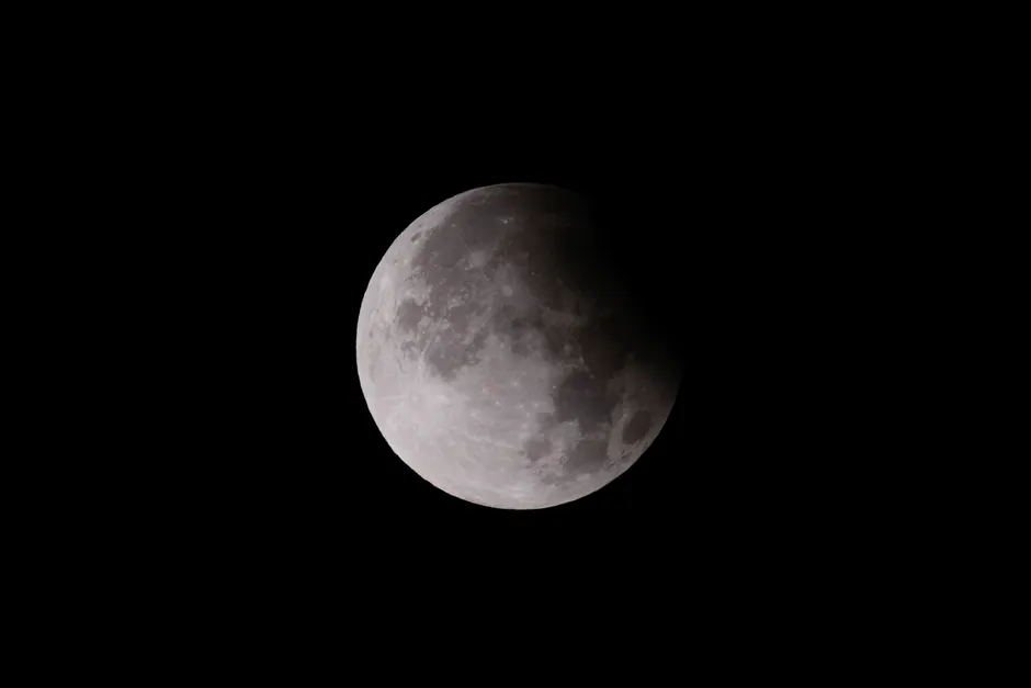 Foto de close-up de um eclipse lunar, mostrando a superfície da lua com jogo de sombras.
