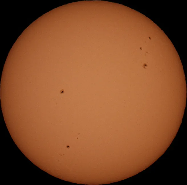 Visão aproximada do sol mostrando manchas solares visíveis contra um fundo claro.
