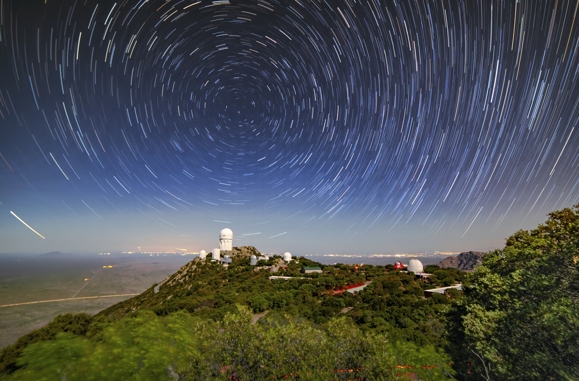 Although this appears to be a daytime scene, star trails circle and illuminate the night sky in this long-exposure photo of Kitt Peak National Observatory (KPNO), a Program of NSF NOIRLab. The telescope visible at the highest peak is the Nicholas U. Mayall 4-meter Telescope and almost directly above it, at the center of the concentric star trails, sits the North Star, Polaris. As the Earth turns and the stars appear to move through the sky, Polaris remains stationary at the north celestial pole,