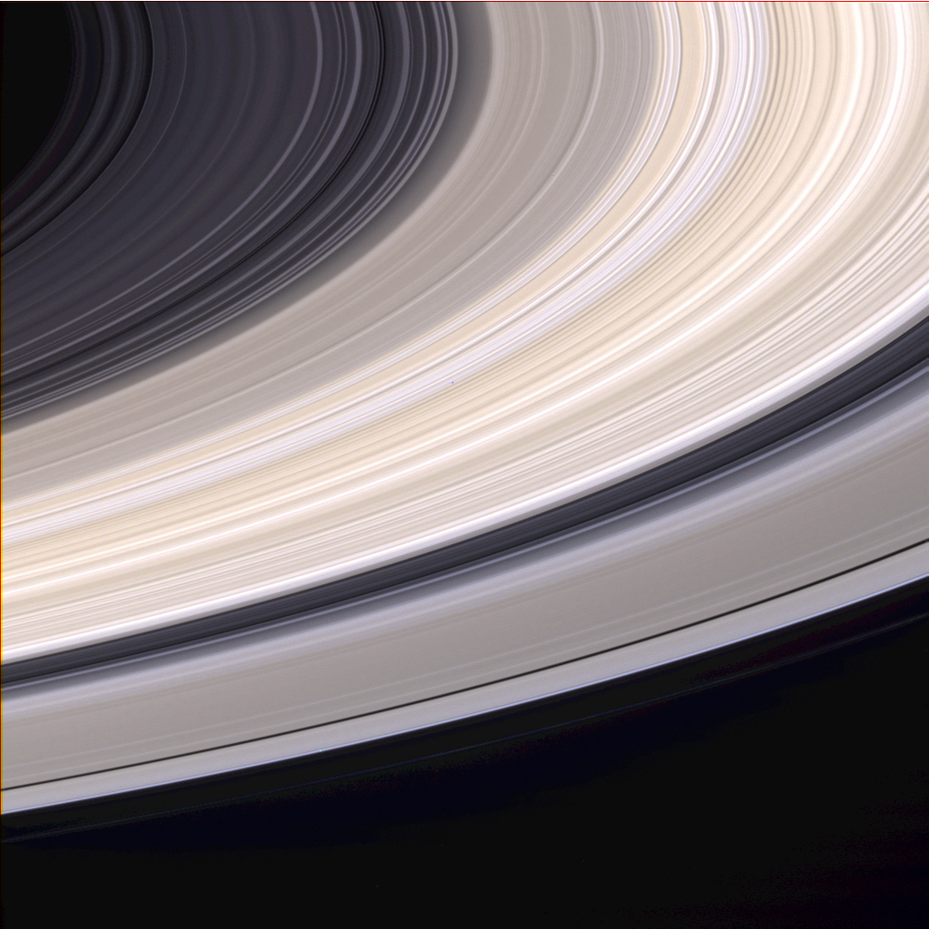 Vista em cor natural dos anéis de Saturno cruzando diagonalmente o quadro, observados pela Cassini de baixo do plano dos anéis; faixas claras e arenosas destacam o anel B.